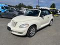 A 2005 Chrysler PT Cruiser convertible in white with a black soft top parked with other vehicles in the background
