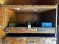 An empty wooden storage cabinet with two open shelves showing some wear, featuring a blue plastic bin on the top shelf and a metal divider on the bottom shelf