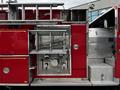 A red 1991 Sutphen Deluge fire truck with compartments and a metal ladder on top visible from the side showing various equipment and controls