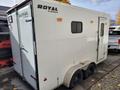 A 2022 Royal Camper trailer with a white exterior featuring the "Royal Cargo" logo on the side two small windows and dual axles