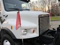 A white 2006 Freightliner M2 106 truck with a silver grille and red flags attached to the side