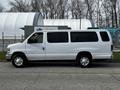 A white 2014 Ford Econoline van with a long body and large windows parked on a street