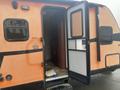 2015 Winnebago Of Indiana Travel Trailer with an open door revealing a glimpse of the interior and an orange exterior with black accents