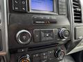 A black dashboard panel of a 2018 Ford F-150 with control knobs for volume and tuning alongside climate control buttons and a display screen showing radio information
