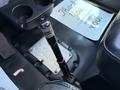A black gear shift lever is positioned next to a textured floor mat in a vehicle interior