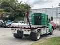 A green 2013 Kenworth T370 flatbed truck with a black bed and red winch hooks is parked with its rear visible