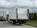 A white 2017 Hino 338 truck with a large box cargo area is parked, showing its rear view and reflective striping on the back panels