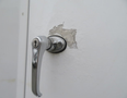 A close-up of a silver door handle on a white surface with chipped paint exposing the underlying material