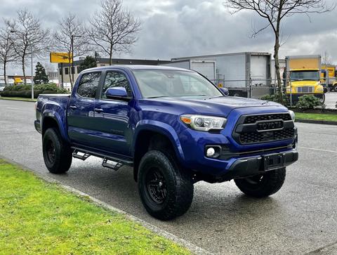 A blue 2022 Toyota Tacoma truck parked on a street with a black grille and large wheels