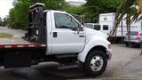 A white 2008 Ford F-750 flatbed truck with a black bed and side steps parked with the cab facing right