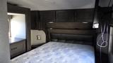 Interior of a 2021 Grand Design Recreational 311BHS featuring a queen bed with a quilted mattress and dark cabinetry around the sleeping area