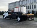 A white 2011 Ford F-750 truck with a flatbed carrying large containers and black toolboxes mounted on the rear