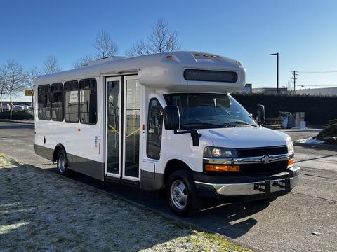 A white 2012 Chevrolet Express shuttle bus with large windows and a raised roof is parked with doors open on the side