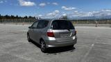 A silver 2006 Honda Fit parked in an open area with its rear visible showcasing its compact design and hatchback style