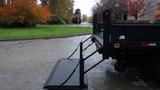 A 2011 Ford F-550 with a loading ramp lowered in the rear positioned on a wet surface surrounded by greenery and autumn trees