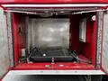 A red fire truck compartment with metal walls and a black flat surface inside featuring wires and a control box mounted on one wall