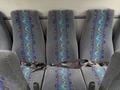 A row of grey fabric seats with blue and green wavy patterns and brown seat belts across the middle