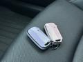 Two car keys, one purple and one pink, resting on a black textured seat surface