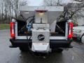 A 2023 Ford F-250 truck bed fitted with a silver salt spreader attached to the rear featuring the name "Fisher" prominently displayed