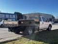 A white 2011 Ford F-350 SD with a flatbed and tool compartments parked on a street