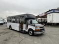 A 2017 Chevrolet Express bus with a white and gray exterior is parked with its door open in a commercial area