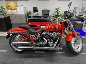 A 2024 Harley Davidson Fat Boy motorcycle in vibrant orange with chrome detailing and a low-profile seat