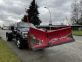 A 2012 Ford F-550 truck with a large red snow plow attached to the front standing on the roadside