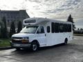 A white 2015 Chevrolet Express bus with multiple windows and a high roof design parked on the road