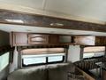 A cabinet with wooden doors above a couch inside a 2013 Outdoor Wind River camper with patterned upholstery and window coverings