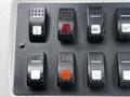 Control panel with several black switches and buttons including red and white ones arranged in two rows