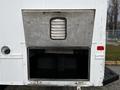A large metallic storage compartment door on the side of a 2006 GMC C5000 is open revealing an empty storage area inside