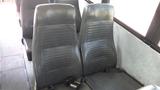 Two black vinyl bus seats with vertical ridges and seatbelts visible in the foreground