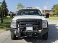 A white 2015 Ford F-550 truck with a black front bumper and a flatbed equipped with a tool rack and lights on top