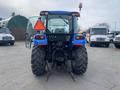A blue 2016 New Holland T475 tractor with large rear tires and a transparent door, featuring a warning light on top and an orange safety triangle attached