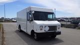 A white 2011 Ford Econoline delivery truck with a boxy shape and a single front window parked in an open area