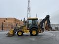 A yellow and black 2011 John Deere 310SJ 4x4 wheel loader with an extended hoe and a 4-in-1 bucket positioned on a construction site