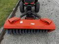 A red rotary broom attachment with blue bristles attached to a tractor's front hitch