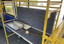 A wooden bench with a gray padded seat attached to a yellow metal frame inside a bus
