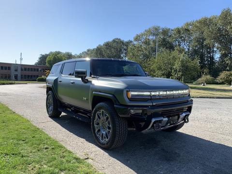 A 2024 GMC HUMMER EV in a matte green finish featuring large wheels and a distinctive front design with LED headlights