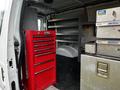 A 2011 Ford Econoline van interior featuring a red tool chest and metal storage boxes against a backdrop of shelves and flooring