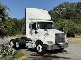 A white 2007 International 9200i truck with a high roof and chrome grille parked on a concrete surface with green foliage nearby