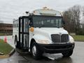 A 2016 International CE300 school bus with a white exterior is parked with its front door open displaying yellow lights on the roof and front fender
