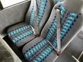 Two blue and gray patterned seats with seat belts inside a bus, featuring a textile design of woven lines in blue and black