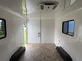 An empty 2025 Shuttle Office interior featuring smooth white walls a door on one side and two seating benches along the sides with a wooden floor