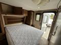 Interior of a 2013 Outdoor Wind River featuring a bed with a white mattress and wooden cabinetry above and beside it