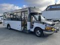 A 2018 Chevrolet Express bus with a white exterior and a gray front end featuring a black grille and headlights, designed for passenger transport with multiple seating inside