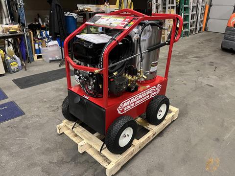 A red 2024 Magnum 4000 Hot Water Pressure Washer with large wheels a pressure hose connection and various gauges mounted on a wooden pallet