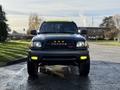 A 2004 Toyota Tacoma with a dark exterior featuring a light bar on the roof and yellow fog lights on the front bumper