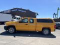 A yellow 2013 Chevrolet Silverado 1500 pickup truck with an extended cab and a cap on the bed facing sideways