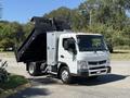 A white 2015 Mitsubishi Fuso FE dump truck is parked with its bed raised, showcasing its loading capabilities